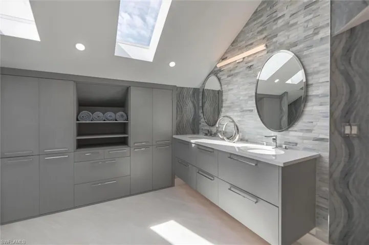 Bathroom featuring double sink vanity, backsplash, and lofted ceiling with skylight