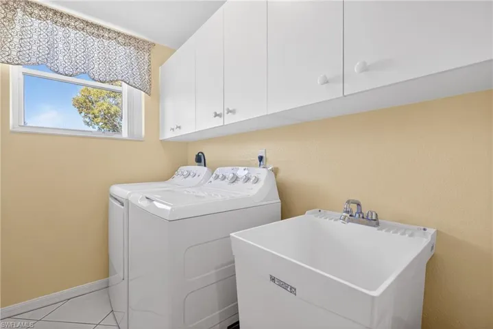 Laundry room with upgraded upper cabinets, washer, dryer laundry sink/tub, window, and white tile flooring