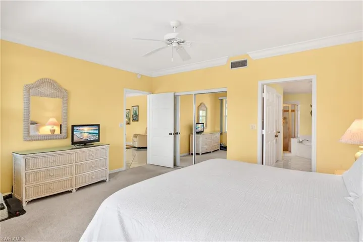 Master bedroom with crown molding, light carpet, a ceiling fan, walk-in closet, and ensuite bath