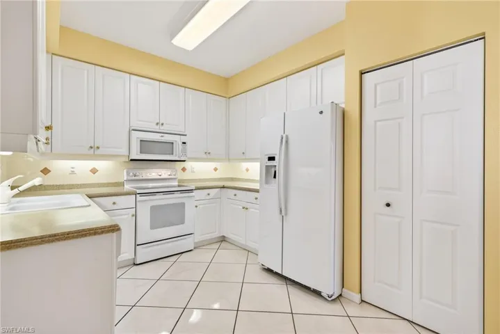 Kitchen featuring white appliances, white cabinets, under cabinet lighting, pantry, white tile patterned floors