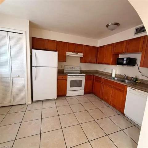 Kitchen featuring white appliances, brown cabinets, light tile patterned flooring, and dark countertops