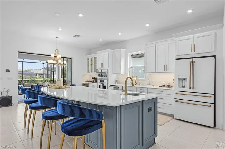Kitchen with stainless steel appliances, white cabinets, a center island with sink, backsplash, and light countertops