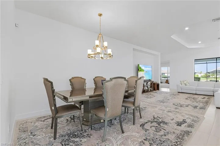 Dining room with a chandelier, tile patterned flooring, recessed lighting, and a tray ceiling