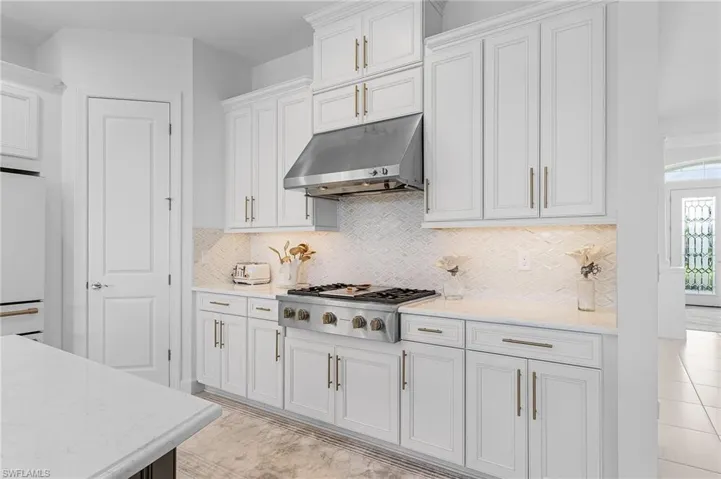Kitchen with under cabinet range hood, stainless steel gas stovetop, white refrigerator, light countertops, and tasteful backsplash