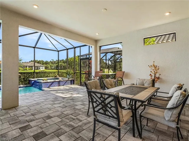 View of patio with outdoor dining area, glass enclosure, and a pool with connected hot tub
