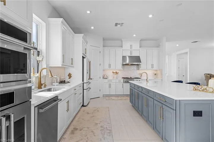 Kitchen featuring stainless steel appliances, under cabinet range hood, white cabinetry, light countertops, and recessed lighting
