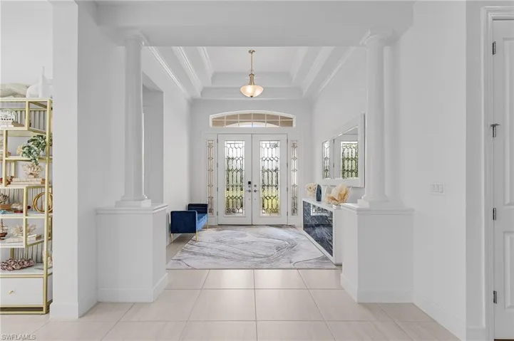 Tiled foyer with decorative columns, ornamental molding, french doors, and a tray ceiling