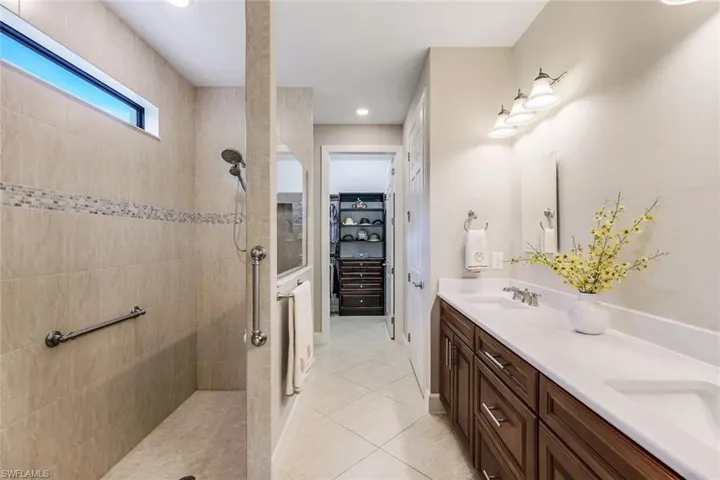 Bathroom featuring tiled shower, tile flooring, double sink, and vanity with extensive cabinet space