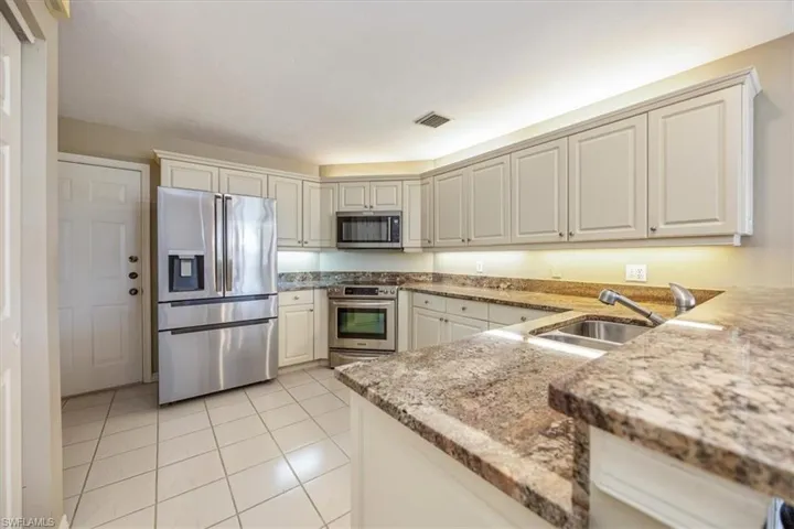 Kitchen with stainless steel appliances, sink, light stone countertops, and light tile patterned flooring