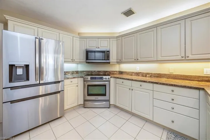 Kitchen with light tile patterned floors, stone countertops, stainless steel appliances, and white cabinets