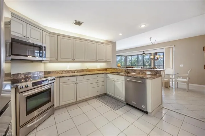 Kitchen featuring kitchen peninsula, dark stone countertops, appliances with stainless steel finishes, and a chandelier