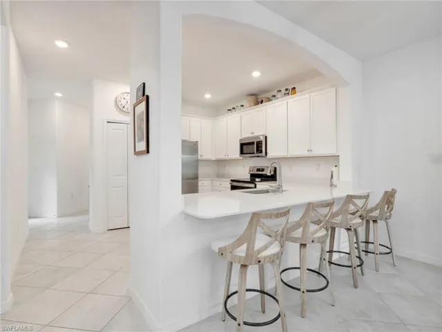 Kitchen featuring an arched passthrough, recessed lighting, white cabinetry, stainless steel appliances, and a breakfast bar with seating for four