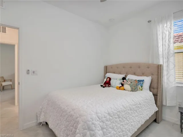 Bedroom featuring a textured upholstered headboard, light-toned tiled flooring, baseboard trim, and a window with blinds and sheer curtains