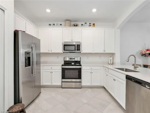 Kitchen featuring white shaker-style cabinetry, light-toned countertops, and stainless steel appliances including a refrigerator, range, microwave, and dishwasher