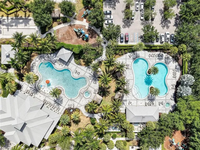 Community amenities featuring two freeform swimming pools, surrounding lounge areas, multiple mature palm trees, and a shaded playground