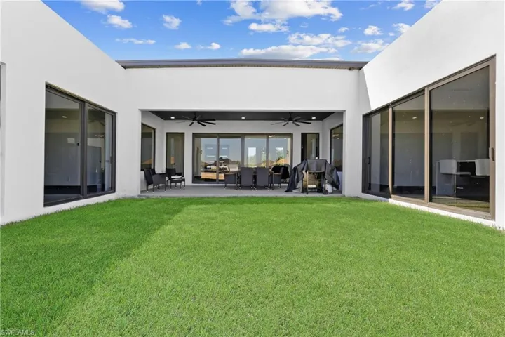 Back of house with a ceiling fan, stucco siding, a lawn, and outdoor lounge area