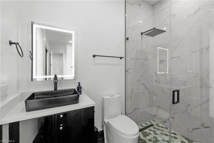 Full bathroom featuring a marble finish shower, toilet, and vanity