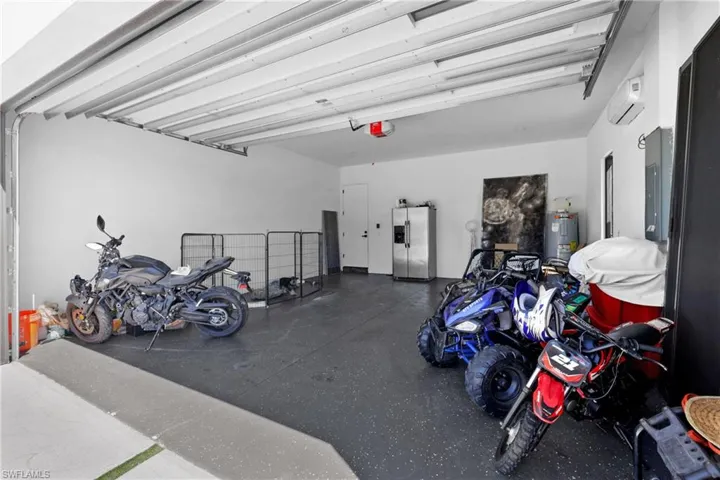Garage featuring stainless steel fridge with ice dispenser, water heater, a garage door opener, and a wall unit AC