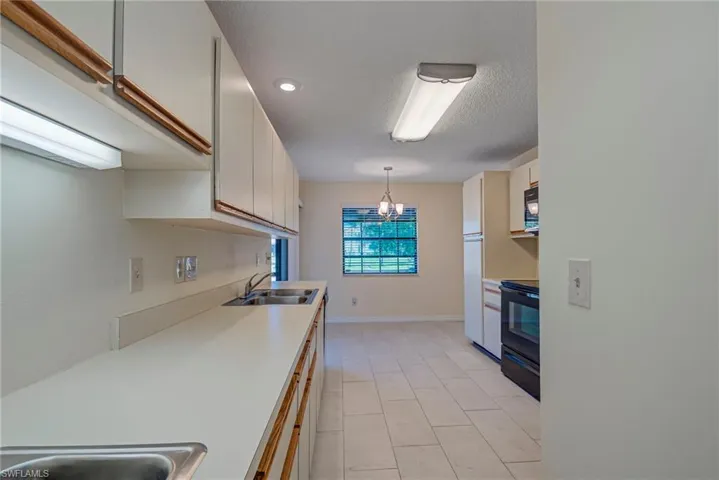 Kitchen with white cabinetry, light countertops, pendant lighting, black appliances, and a chandelier