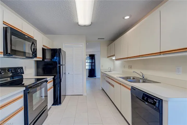 Kitchen featuring black appliances, a textured ceiling, light countertops, and white cabinetry
