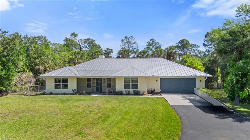 Ranch-style home featuring fence, a front yard, metal roof, a garage, and driveway