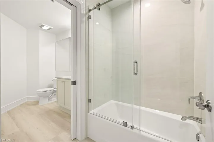 Full bath featuring vanity, toilet, bath / shower combo with glass door, visible vents, and wood finished floors