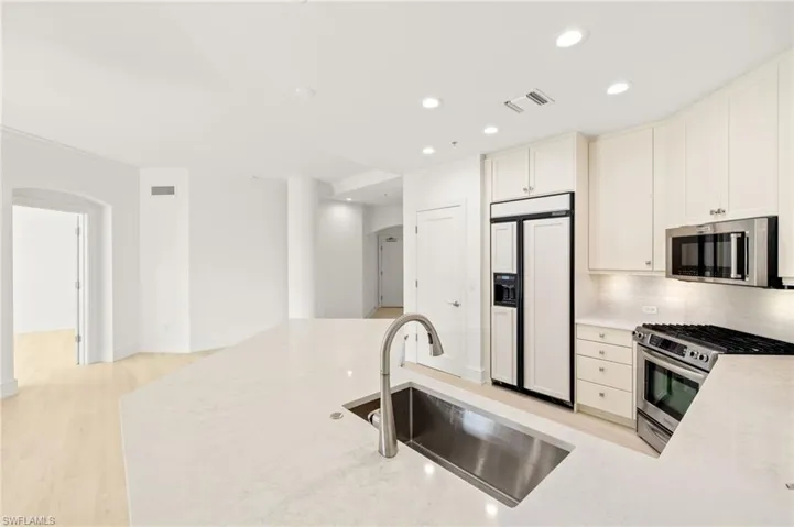 Kitchen featuring a sink, backsplash, appliances with stainless steel finishes, visible vents, and arched walkways