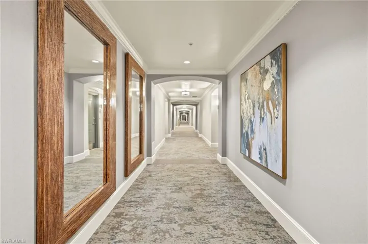 Hall with carpet flooring, arched walkways, crown molding, and baseboards