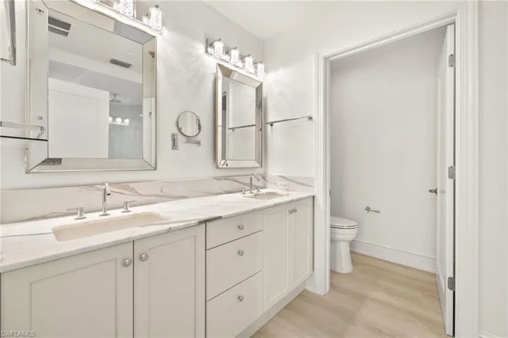Bathroom with toilet, a sink, double vanity, and wood finished floors