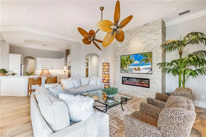 Living room with arched walkways, a ceiling fan, ornamental molding, a fireplace, and light wood-style floors