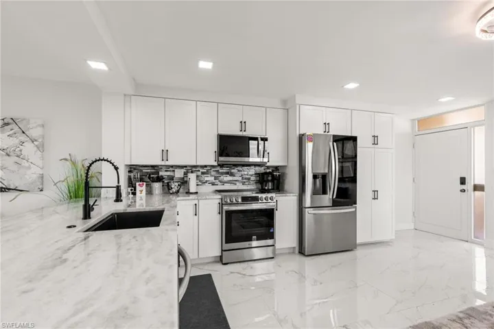 Kitchen featuring appliances with stainless steel finishes, light stone countertops, sink, and white cabinets