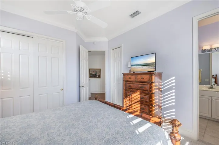 Carpeted Guest bedroom 1 with crown molding, ensuite bath, ceiling fan, and plantation shutters