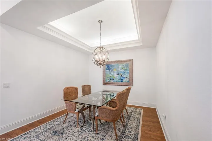 Dining area featuring laminate floors, a tray ceiling, an inviting chandelier, and crown molding