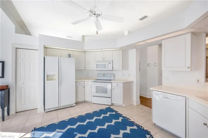Kitchen with ceiling fan, light tile patterned floors, white cabinets, and white appliances