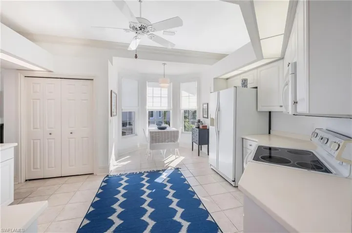 Kitchen with pendant lighting, light tile patterned floors, white appliances, ceiling fan, and white cabinets