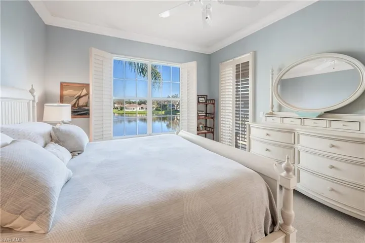 Carpeted Master bedroom with a water view, plantation shutters, ceiling fan, and crown molding