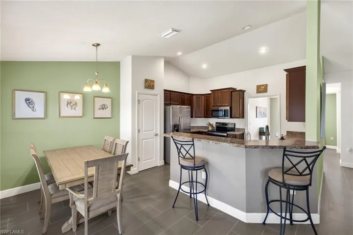 Kitchen featuring appliances with stainless steel finishes, lofted ceiling, a peninsula, a breakfast bar area, and a chandelier