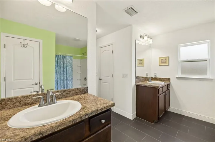 Full bath featuring baseboards, two vanities, a shower with shower curtain, and tile patterned floors