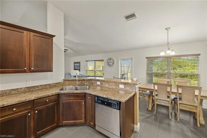 Kitchen with stainless steel dishwasher, a sink, light tile patterned floors, a peninsula, and a chandelier