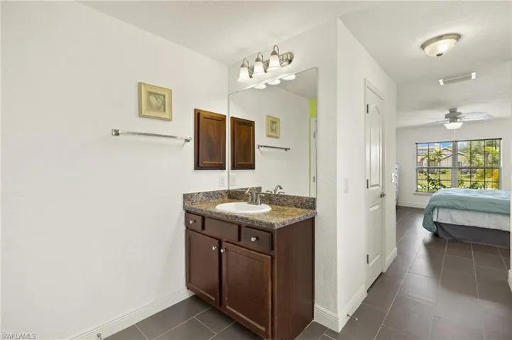 Ensuite bathroom featuring vanity, tile patterned floors, baseboards, and ceiling fan