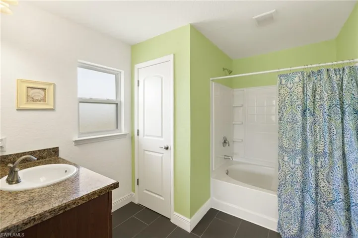 Full bathroom with baseboards, vanity, shower / bath combo with shower curtain, and tile patterned flooring