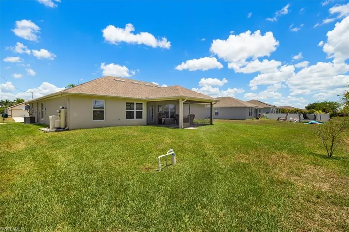 Back of house with stucco siding, a lawn, and central air condition unit