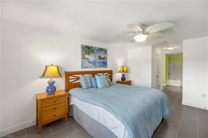 Tiled bedroom with baseboards, ensuite bathroom, and ceiling fan