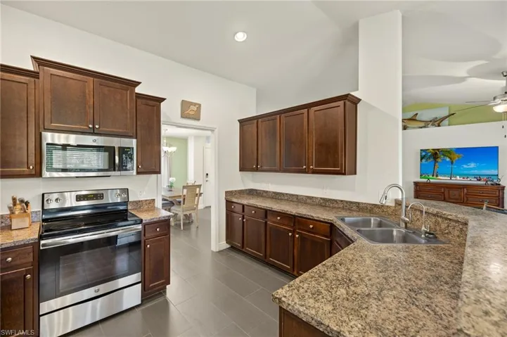 Kitchen with stainless steel appliances, a sink, a ceiling fan, a chandelier, and dark brown cabinets