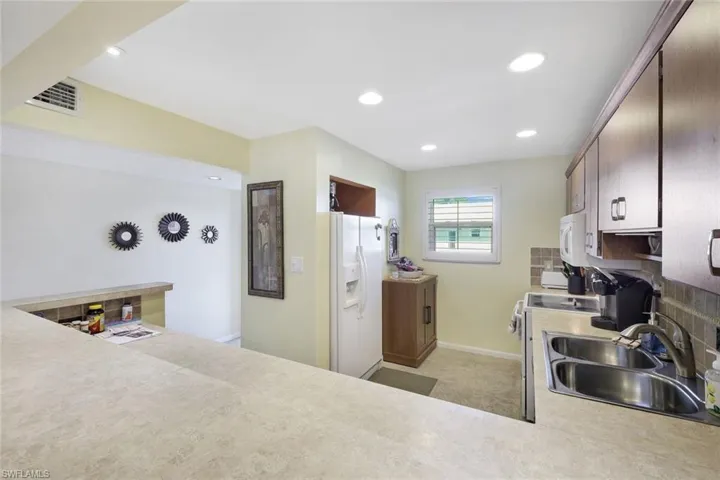 Kitchen with white appliances, tasteful backsplash, visible vents, light countertops, and a sink