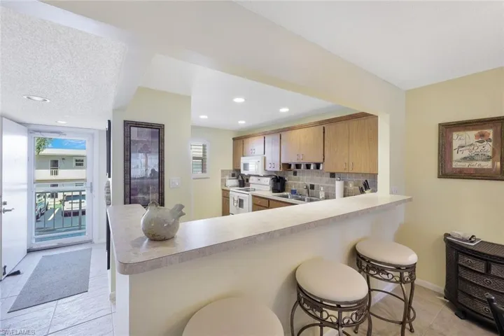 Kitchen featuring a breakfast bar, white appliances, light countertops, backsplash, and a sink