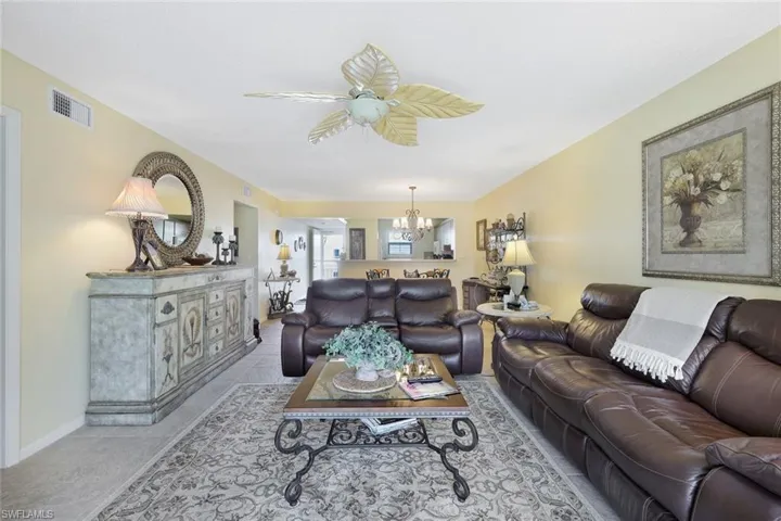 Living room featuring ceiling fan with notable chandelier, light tile patterned floors, baseboards, and visible vents