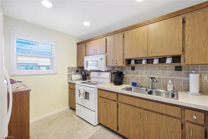 Kitchen featuring white appliances, tasteful backsplash, open shelves, light countertops, and a sink