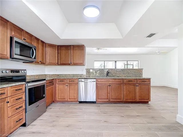 Kitchen with wood finish cabinetry, stainless steel appliances, light stone countertops, wood finish floors, and a peninsula