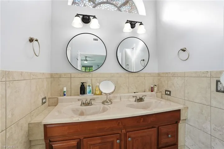 Full bath featuring tile walls, double vanity, wainscoting, and a ceiling fan